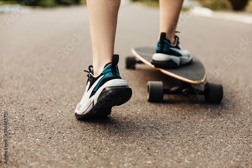 Close-up of female feet wearing sneakers, skating on long board.
