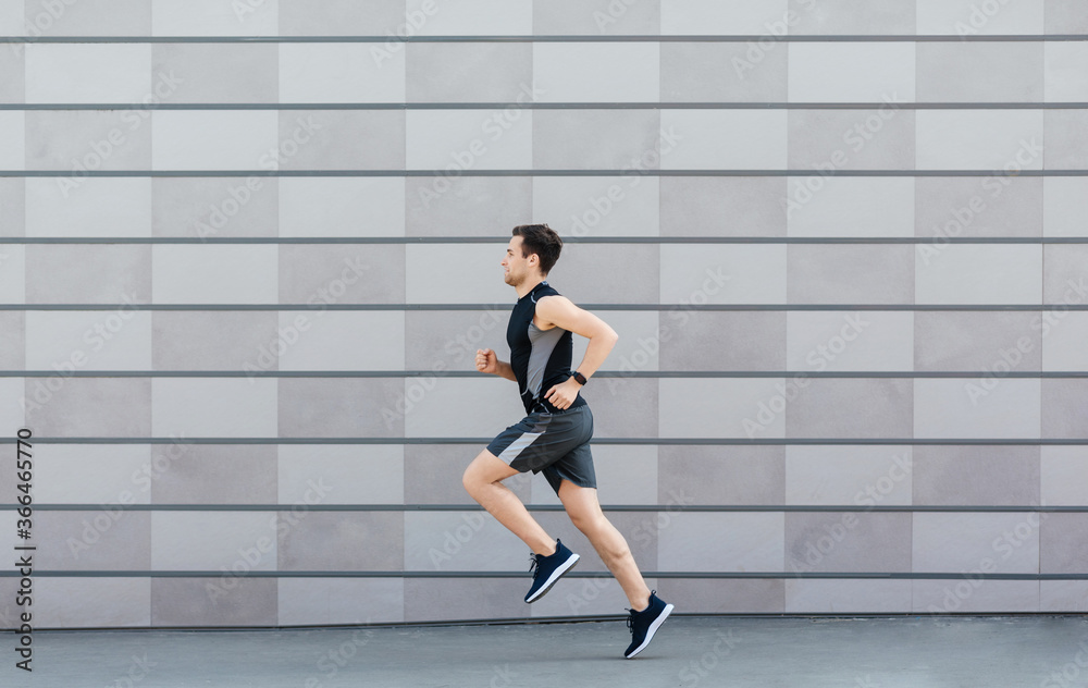 Jogging for health. Man with fitness tracker runs on gray wall background