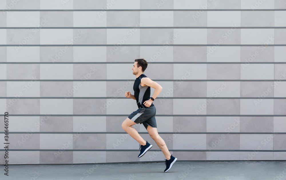 Naklejka premium Jogging for health. Man with fitness tracker runs on gray wall background