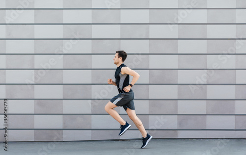 Jogging for health. Man with fitness tracker runs on gray wall background