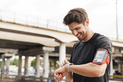Image of athletic smiling sportsman using smartwatch while working out