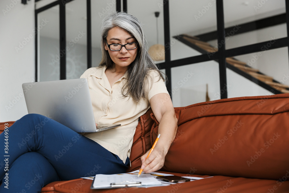Photo of adult asian woman working with laptop and making down notes Photo of adult asian woman working with laptop and making down notes