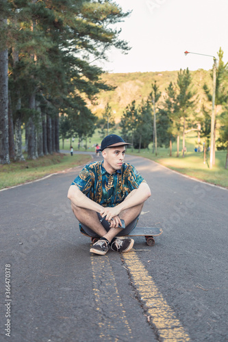 Cool skateboarder sitting on the road. He has his smartphone and a tool in his hand.  Concept of relaxation, enjoyment.