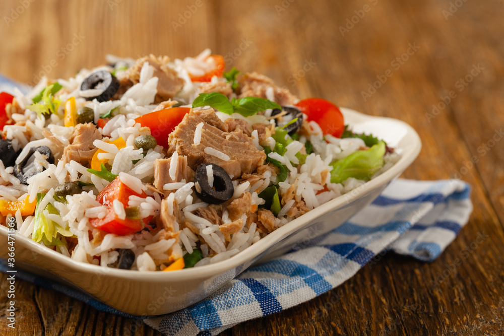 Italian tuna salad with rice, olives and capers. Front view. Natural wooden background.