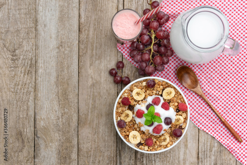 Oatmeal with raspberries, grapes, banana and a glass of yogurt on a wooden background. Breakfast porridge with berries. Top view. Copy space.