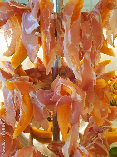 Italian food  sliced raw ham with melon slices hanging in tiers on a stand.