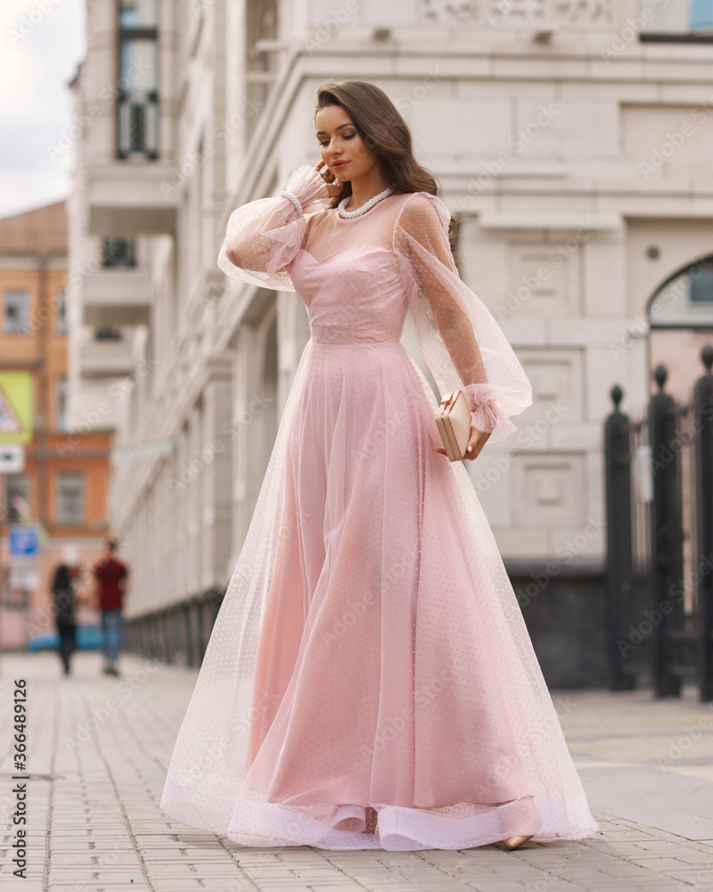 Fototapeta premium Young beautiful woman wearing long pink dress. Outdoor fashion full length portrait.