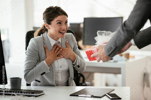 Young businessman giving his colleague present in office. Young man suprise beautiful businesswoman in office. 