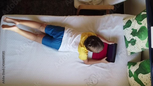 Happy siblings lying on sofa at home and playing with pc tablet together