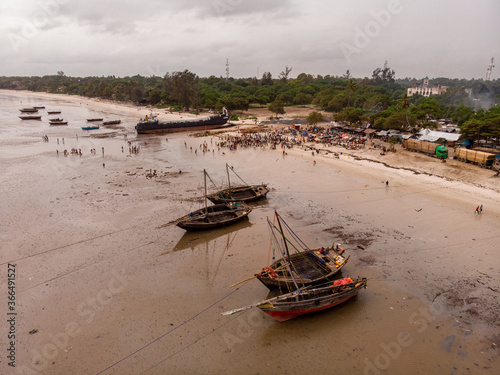 An aerial shot from Bagamoyo, Tanzania. Indian Ocean Coast with Vessels and Crowd of people Carrying Catch from fishermans boats at Low Tide