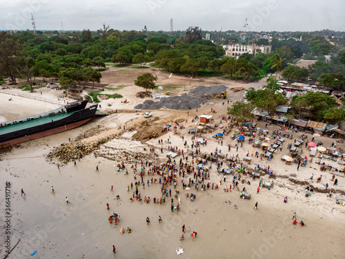 An aerial shot from Bagamoyo, Tanzania. Indian Ocean Coast with Vessels and Crowd of people Carrying Catch from fishermans boats at Low Tide