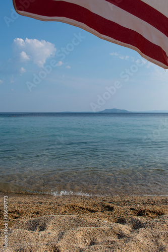 Sandy tropical beach with umbrella and island in the background. Wallpaper, copy space, clear water.