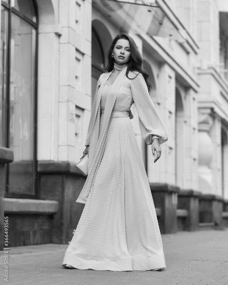 Obraz premium Fashion outdoor portrait. Young stylish woman in long pink evening dress walking at city street on a summer day. Full length