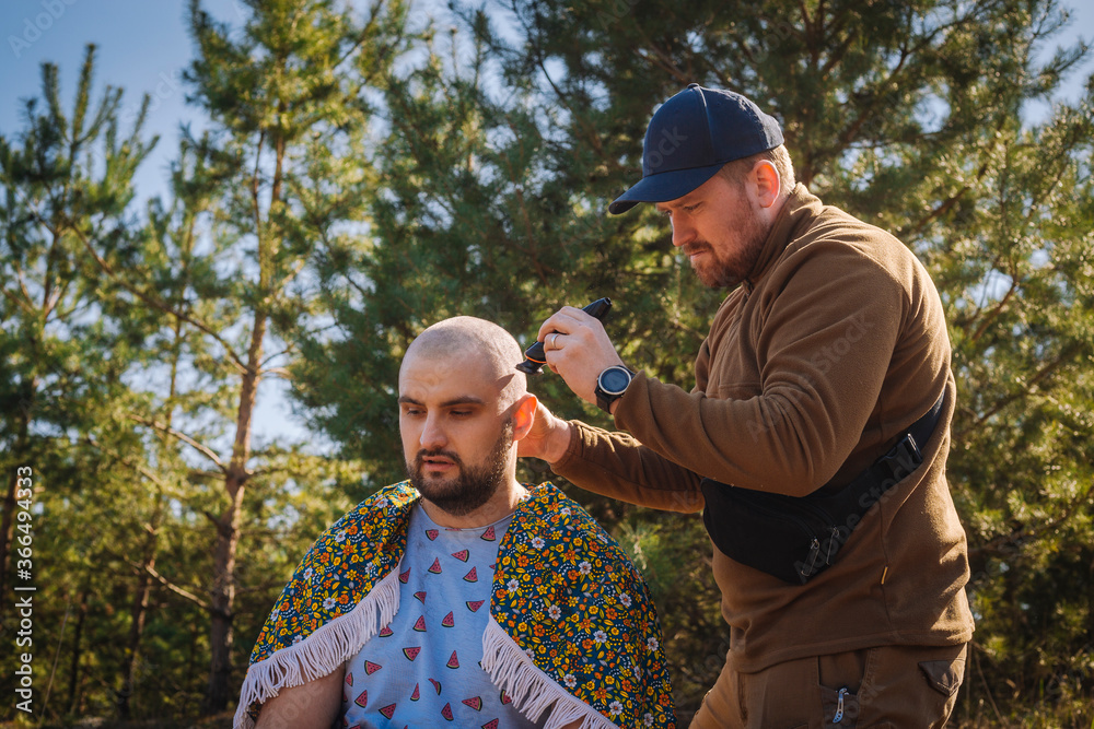 Fototapeta premium Tough red bearded guy shaving bold the other man outdoors in the pine forest