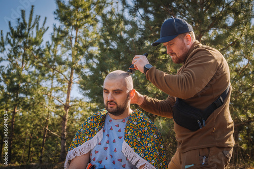 Tough red bearded guy shaving bold the other man outdoors in the pine forest © honey_inside