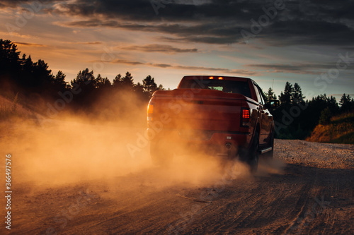 Pickup truck in motion on a country road with clouds of dust. An SUV is driving fast during sunset on a rural gravel road with a lot of dust. fast moving car photo