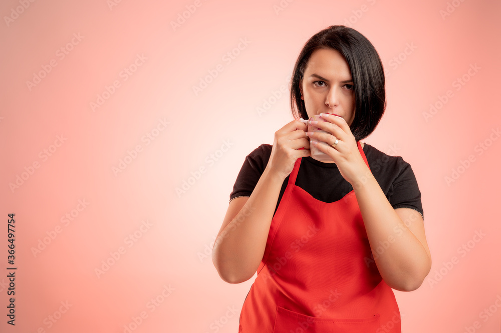 Woman employed at supermarket with red apron and black t-shirt drink coffee from the cup Woman employed at supermarket with red apron and black t-shirt drink coffee from the cup