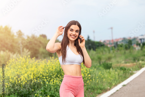 Portrait of a young woman in sportswear talking on phone outdoors while taking break between training, © Graphicroyalty