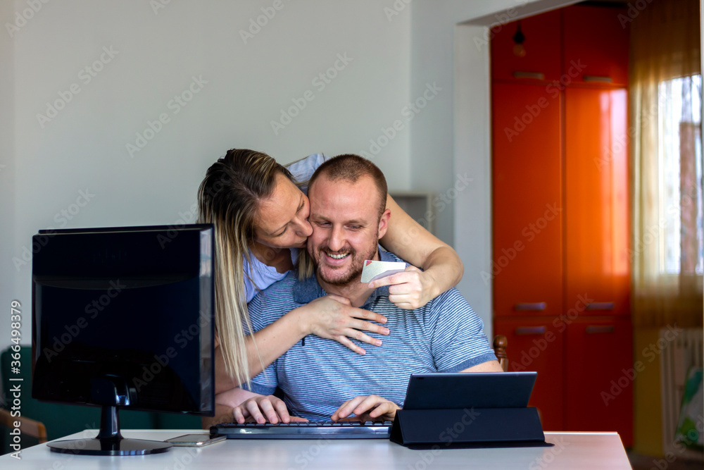 Shot of a young happy woman hugging her smiling husband while he uses a tablet for online shopping on the table at home.Young couple using a digital tablet and credit card in te living room.Copy space Shot of a young happy woman hugging her smiling husband while he uses a tablet for online shopping on the table at home.Young couple using a digital tablet and credit card in te living room.Copy space