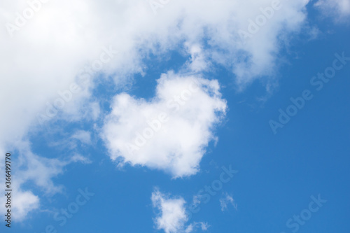 Fluffy white clouds float across the blue sky on a clear sunny summer or spring day. Background sky. Heart shaped cloud. Low angle view