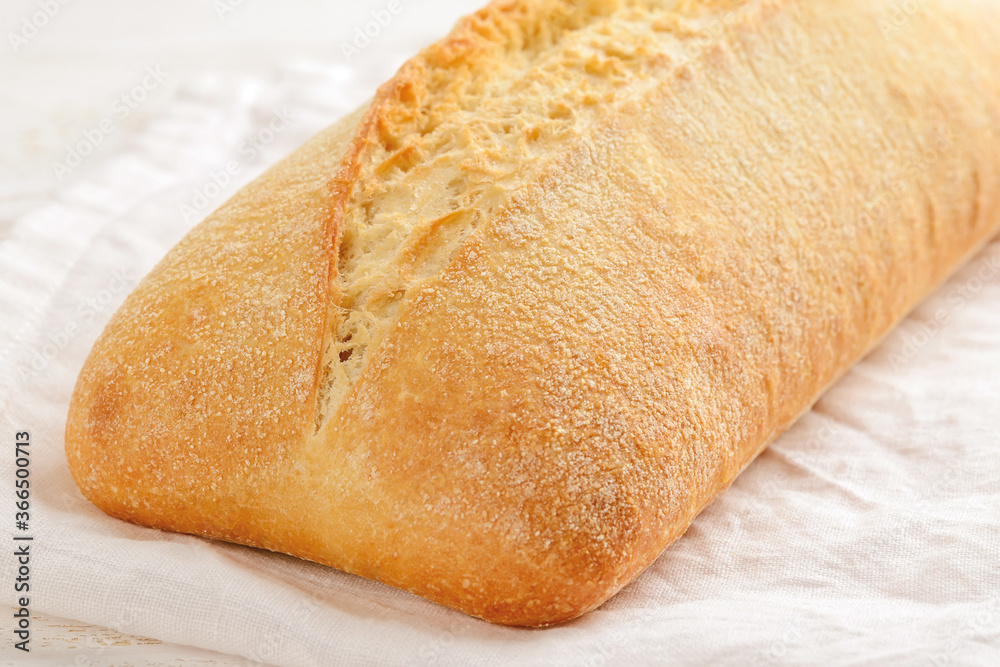 Close-up of whole fresh tasty ciabatta bread on a white linen napkin over a wooden table. Traditional Italian cuisine. Baking wheat bread with yeast or sourdough.