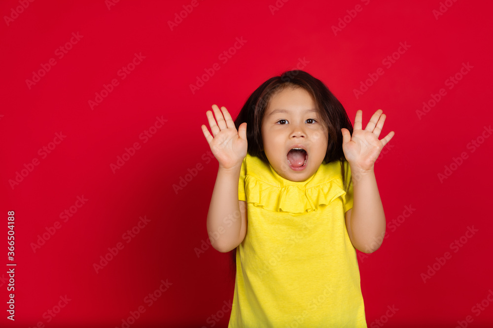 Surprising. Beautiful little girl isolated on red background. Half-lenght portrait of happy child gesturing. Cute asian girl in yellow wear. Concept of facial expression, human emotions, childhood. Surprising. Beautiful little girl isolated on red background. Half-lenght portrait of happy child gesturing. Cute asian girl in yellow wear. Concept of facial expression, human emotions, childhood.