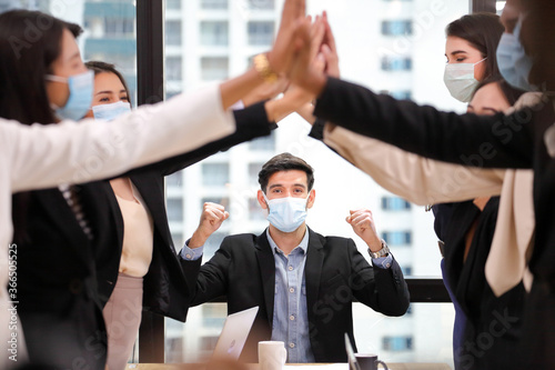 Business people wearing facial mask for new normal and social distancing policy doing high five to the new project after coronavirus in order to survive and avoiding bankruptcy photo