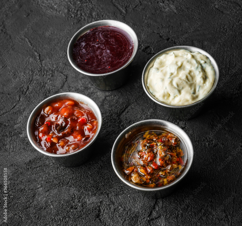 Set of different sauces, mayonnaise, hot pepper, tomato garlic sauce, berry spicy sauce in bowl on black stone background Set of different sauces, mayonnaise, hot pepper, tomato garlic sauce, berry spicy sauce in bowl on black stone background