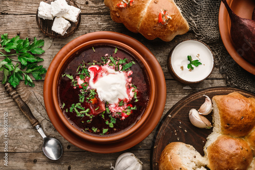 Ukrainian and Russian traditional beet root soup or borscht in bowl with rib eye meat, sour cream, buns, goat cheese, garlic, parsley on a wooden rustic background. Healthy food, top view