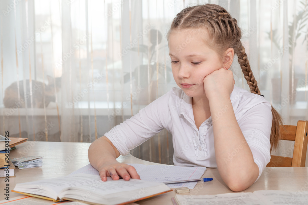 Schoolgirl studying at home. Young girl reading book at the table. Distance and home education concept Schoolgirl studying at home. Young girl reading book at the table. Distance and home education concept