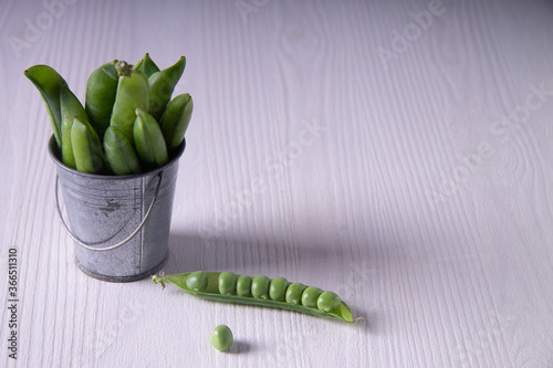 Opened fresh green pea-pod with a tiny zinked bucket filled with pea-pods. White backdrop. Copy space. View from above. photo