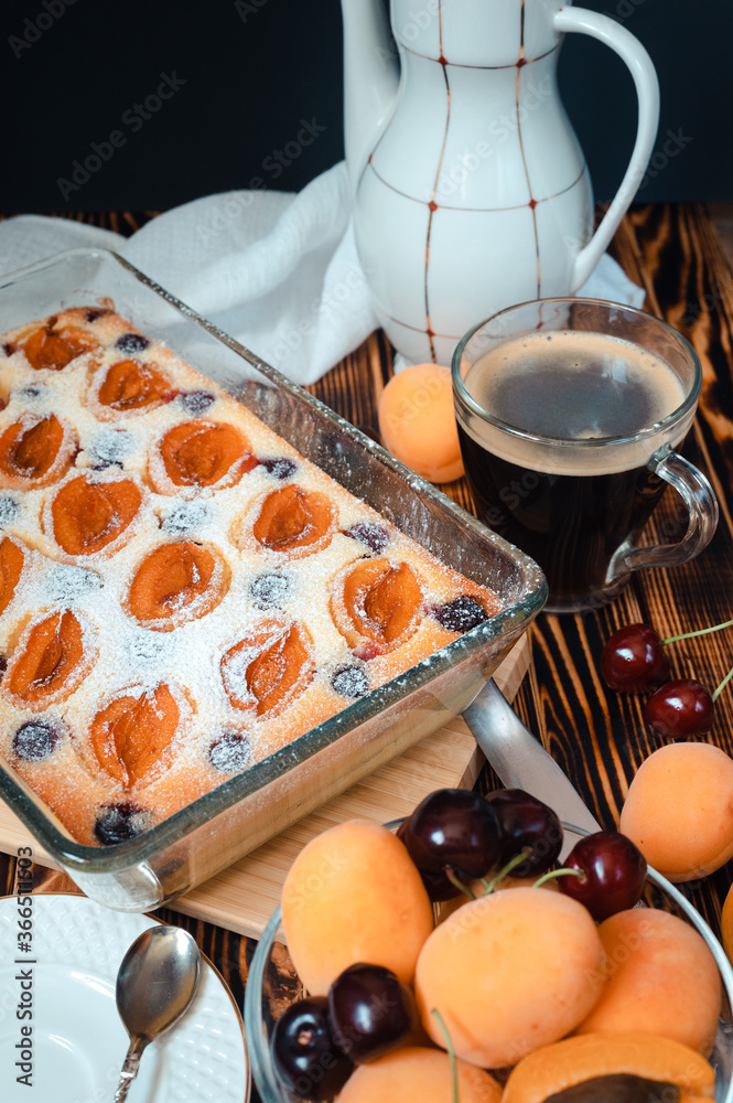Obraz premium cottage cheese apricot casserole decorated with icing sugar, slices of berries on a background of a white coffee pot on a wooden table