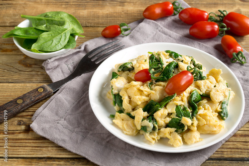 scrambled eggs with spinach and tomatoes on a white plate.