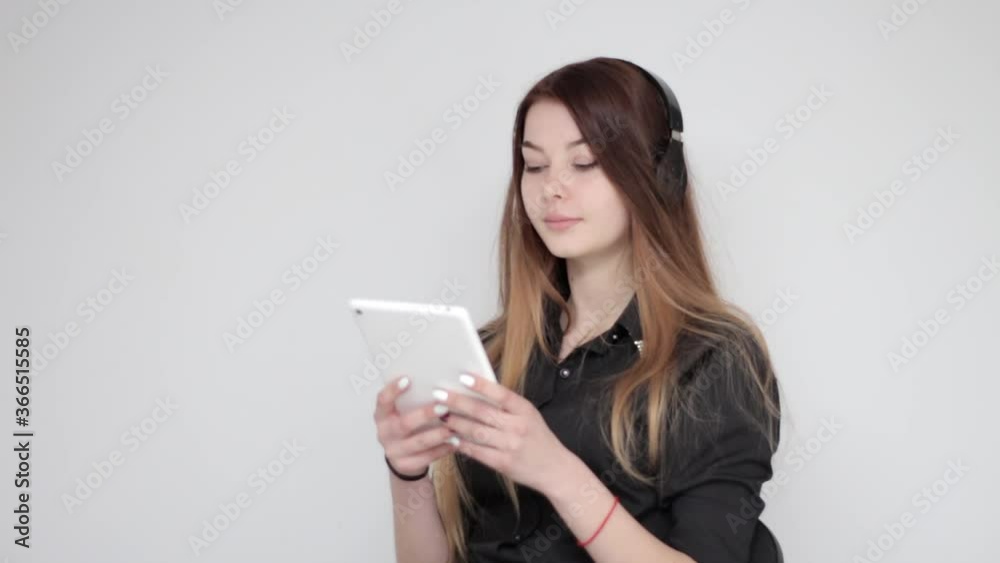Good looking happy young lady with long hair listening to music in wireless headphones and dancing with tablet in hands Good looking happy young lady with long hair listening to music in wireless headphones and dancing with tablet in hands