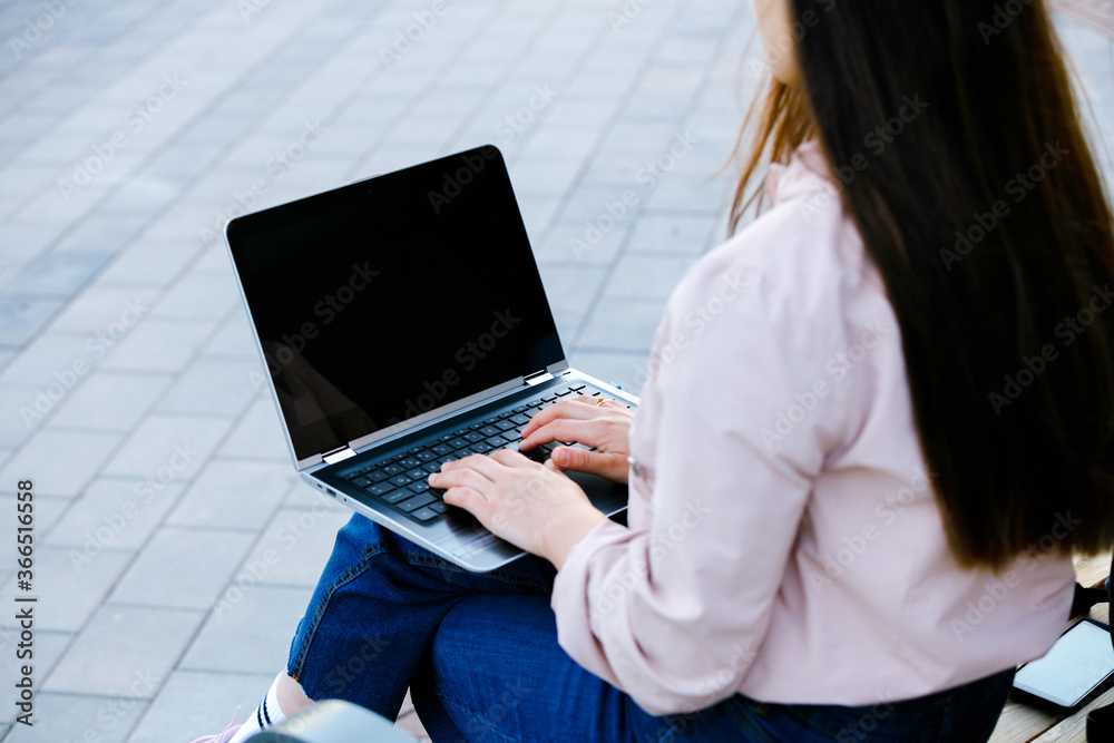 Woman using laptop with black display sitting on bench in city, above view