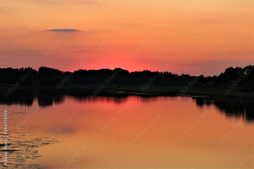 A sunset at a lake with trees on the bank of the lake