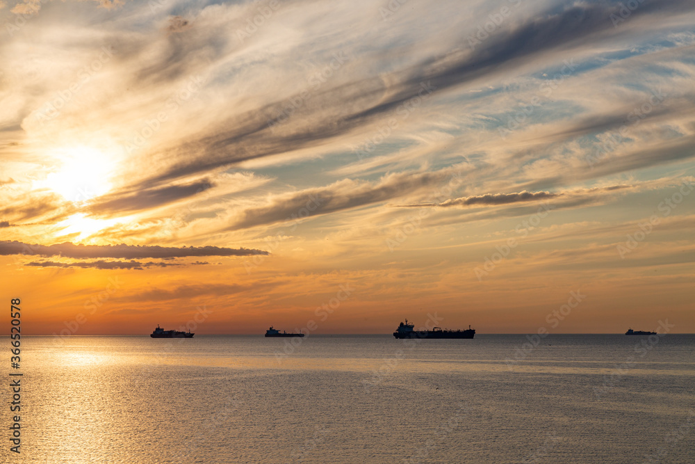 Summer sunset clouds at sky at Baltic sea on horizon cargo ships going to harbour pink orange sky and sunlight reflection on water wave beautiful nature landscape