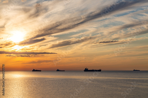 Summer sunset clouds at sky at Baltic sea on horizon cargo ships going to harbour pink orange sky and sunlight reflection on water wave beautiful nature landscape