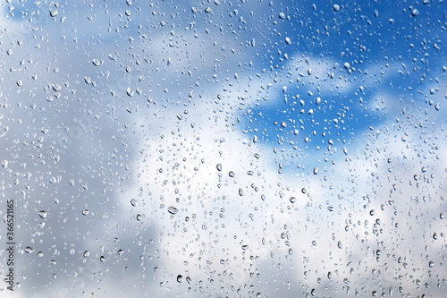 Raindrops on the window glass on blurred background of sky with clouds. Beautiful water drops  rainy weather