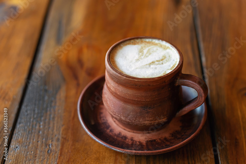 Coffee with milk or cappuccino in brown clay mug on wooden table. 