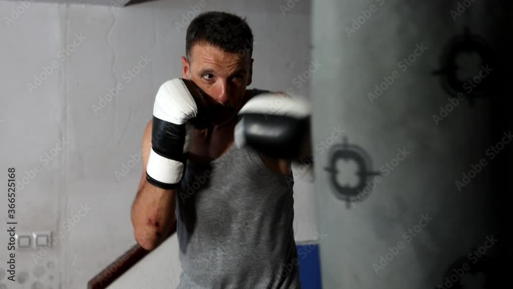 Boxer training hitting punching bag with slopping gloves in slow motion