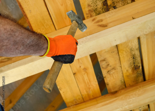 Fotografie close-up - a man holding a hammer in his hands, against a background of wooden b