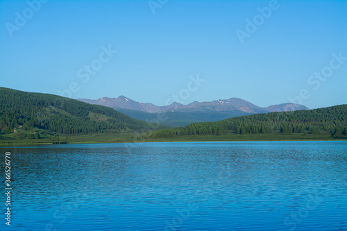 A beautiful mountain lake with reeds surrounded by mountain ranges and impenetrable forests. The lake is high in the Altai mountains