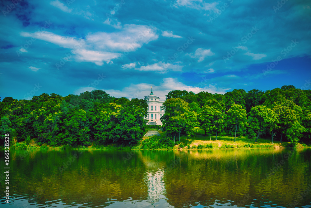 Beautiful landscape of park with manor in summertime. Picturesque place of white Palace with pond and green trees.