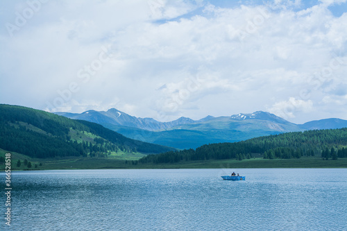A beautiful mountain lake with reeds surrounded by mountain ranges and impenetrable forests. The lake is high in the Altai mountains. Fishing boat on the lake.