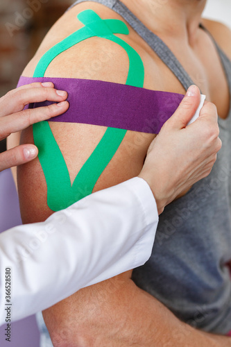 Kinesiology taping. Physical therapist applying kinesiology tape to patient shoulder. Female therapist treating injured shoulder of male athlete. Post traumatic rehabilitation, sport physical therapy.