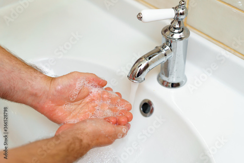 Close up photo of male hands washing with soap above the sink