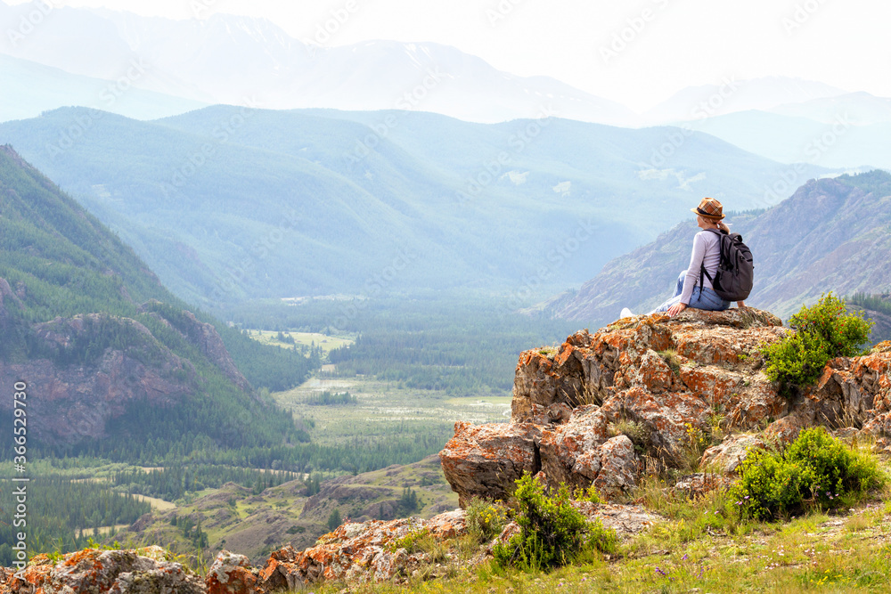  Woman traveler with backpack sitting and looking at view at mountain. Travel, active lifestyle and summer holiday concept.