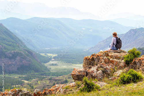  Woman traveler with backpack sitting and looking at view at mountain. Travel, active lifestyle and summer holiday concept.