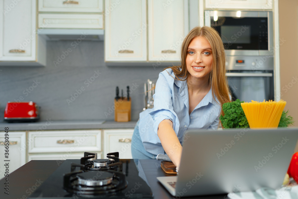 Young blonde woman with long hair using laptop in a kitchen Young blonde woman with long hair using laptop in a kitchen